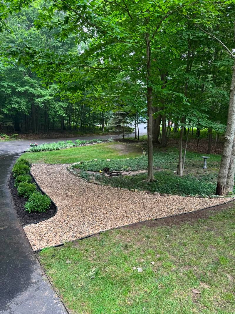 Curved landscape bed with shrubs, steel edging and a gravel path beside a driveway