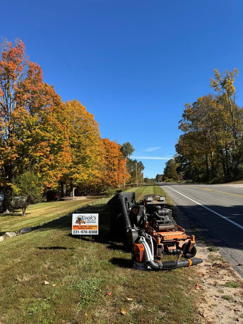 Stand-on mower with a leaf bagger parked by a road lined with fall color