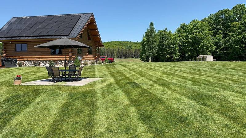 Freshly striped lawn in front of a log home with a shaded patio table